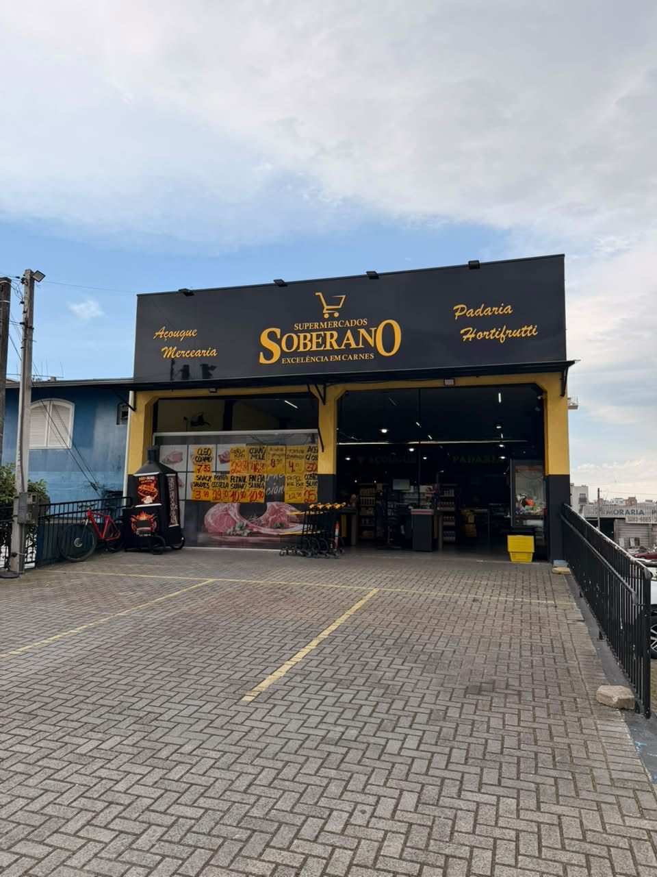 Fachada preta e dourada do Supermercados Soberano, com estacionamento na frente